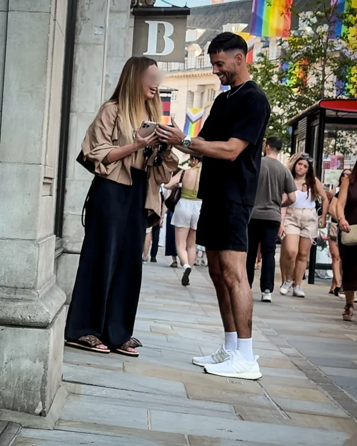 Matt swapping numbers with a woman on a busy street, both looking at her phone.